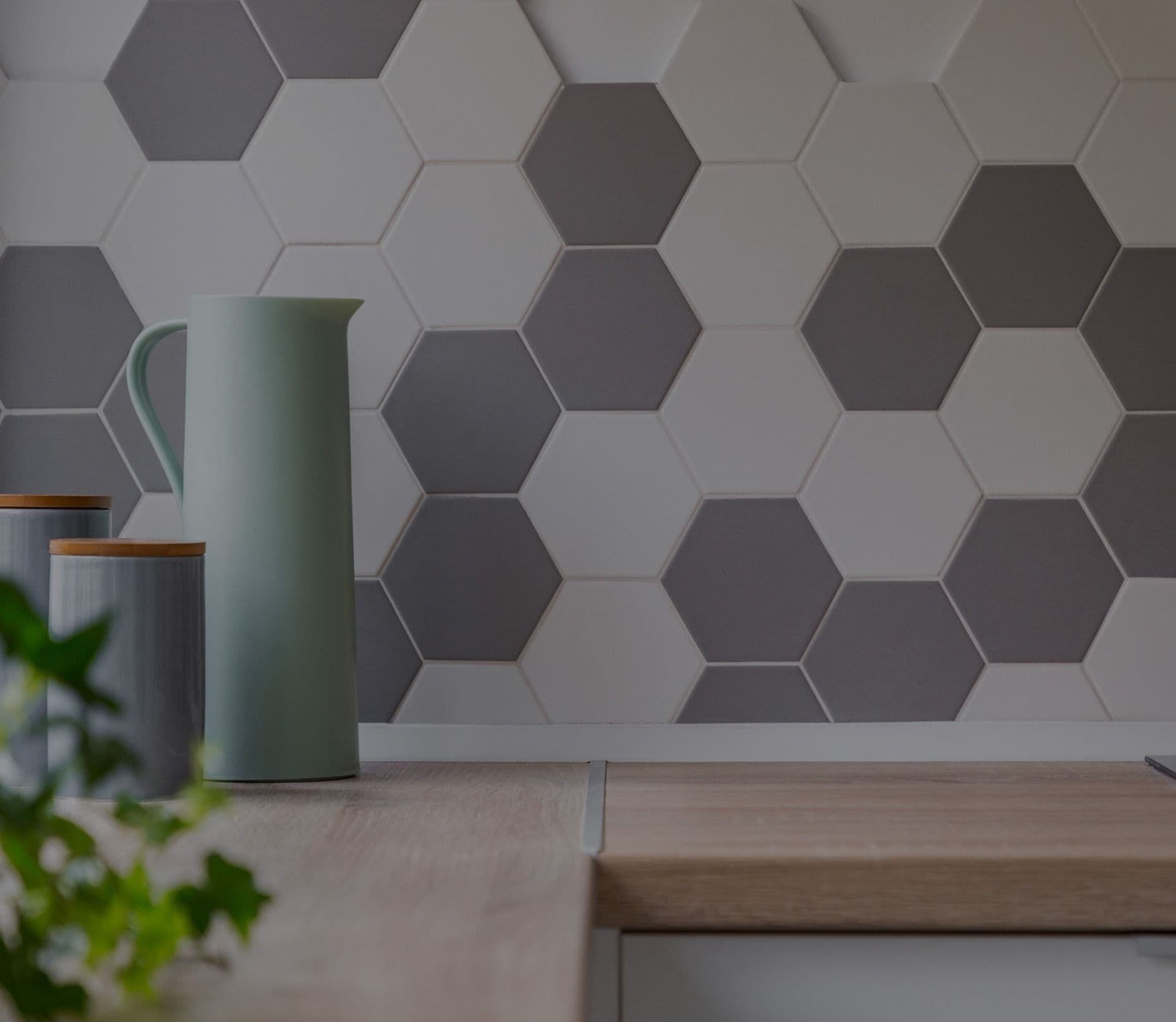 Hexagonal tile backsplash in alternating light and dark gray behind kitchen counter with green pitcher and gray canister